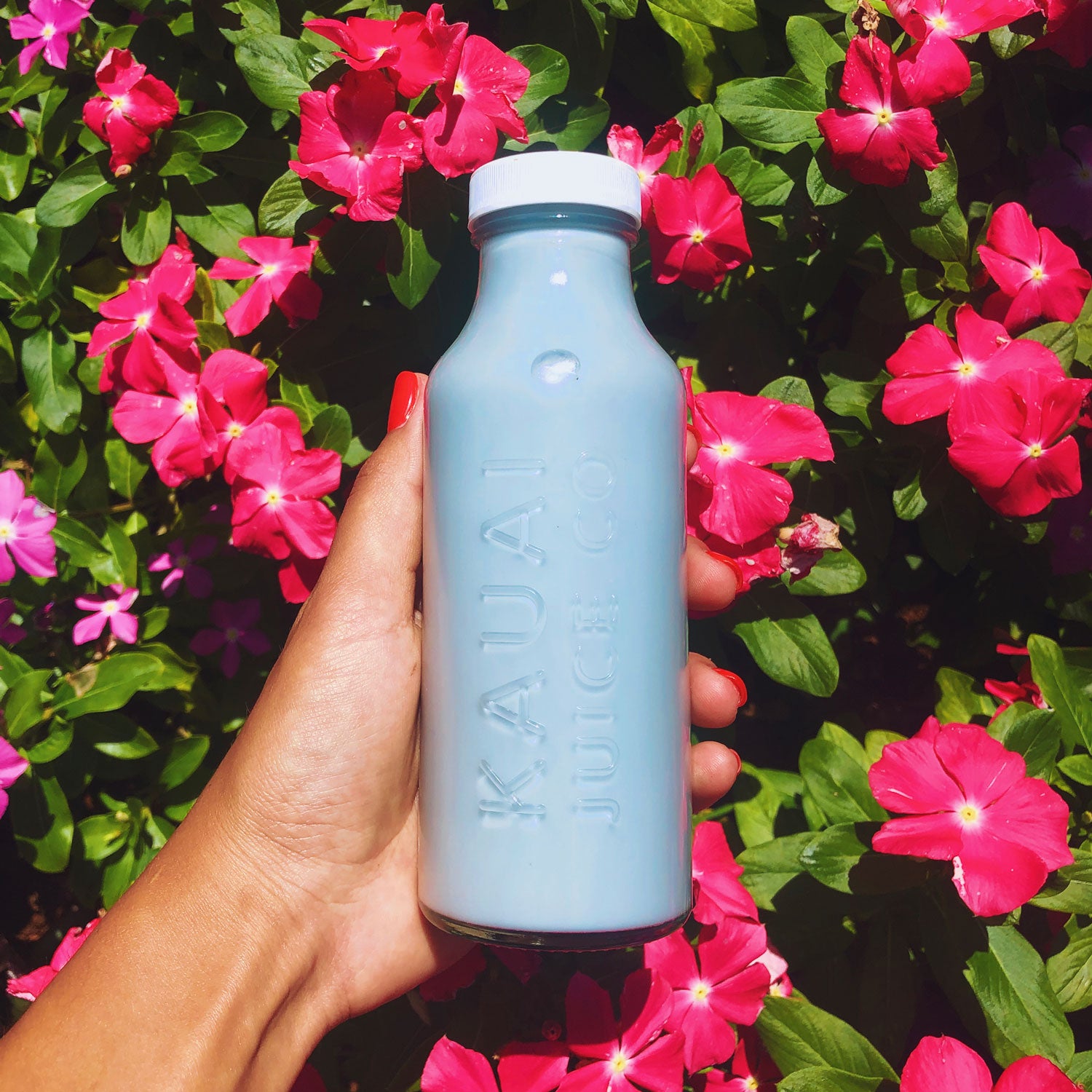 Bottle of fresh juice in front of colorful flowers