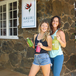 Two staff members holding bottles of juice in front of Kauai Juice store