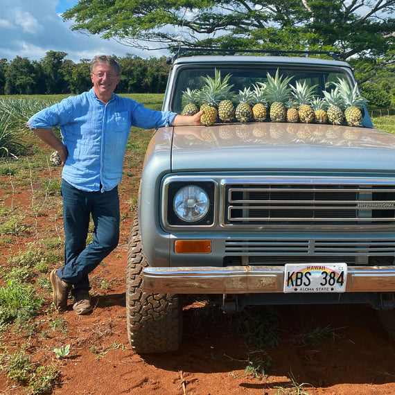 Farmer standing next to truck with pineapples on the hood