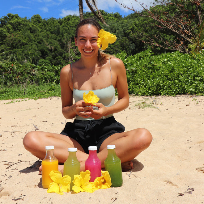 Woman sitting on beach holding a flower with bottles of juice in front of her