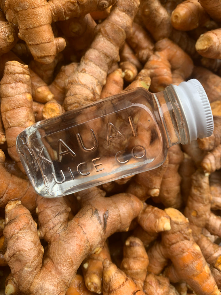 clear 2 oz Kauai Juice Co Bottle on top of fresh ginger pile