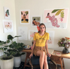 portrait of Margie Rice in front of her artwork, with plants and tropical flowers