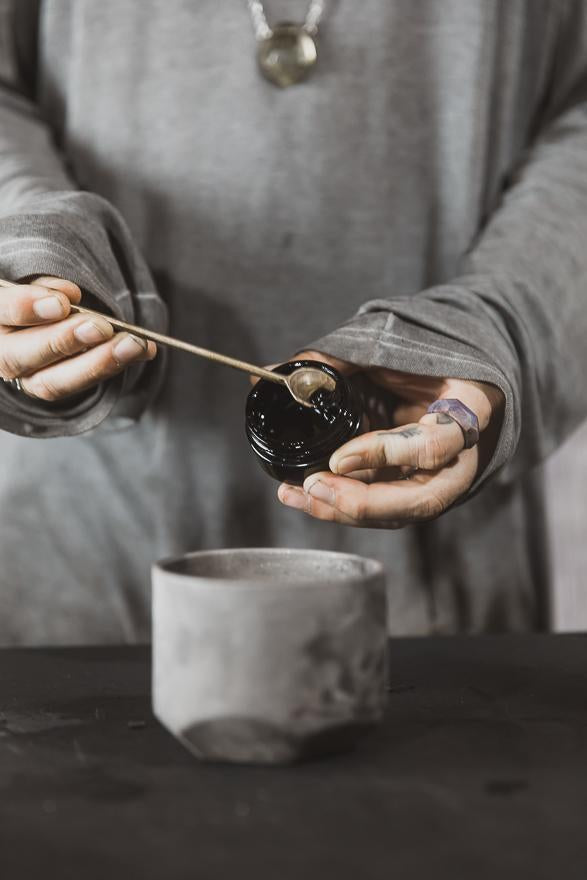 person scooping black jar of resin using small spoon